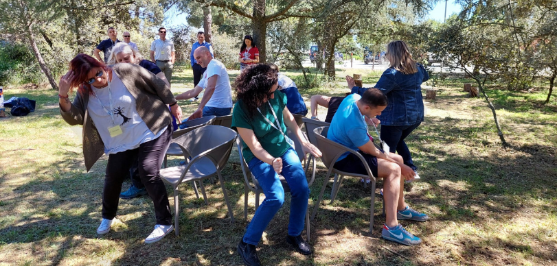 Personnel from Hexagon and the Gil Gayarre Foundation play musical chairs. They are outside in grass, near a tree