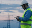 A utility worker standing in front of power lines using mobile technology